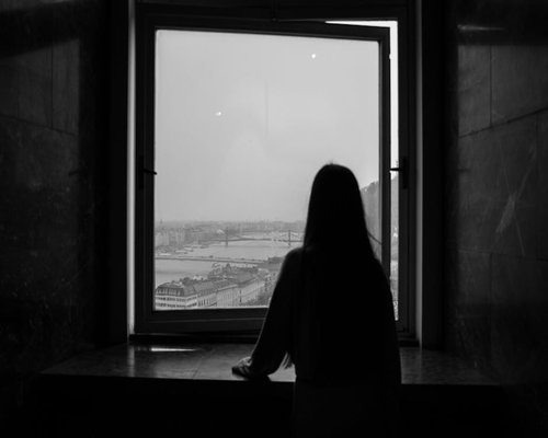 A person relaxing with a book near a window overlooking Budapest at sunset